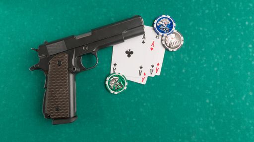 A top shot of a weapon next to some playing cards and dice on a poker board.