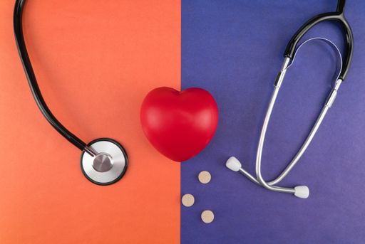 A top shot of a heart-shaped antistress pulse sponge next to a phonendoscope and some pills on a two-colored background.