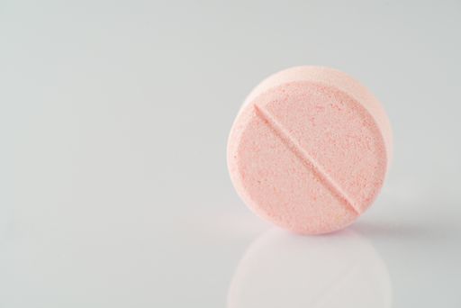 A close-up shot of a pink vitamin pill on a white reflecting surface.