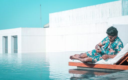 An Indian man looking at his phone while resting on a deck chair near the pool