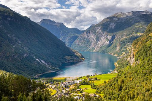 A landscape view of Geirangerfjord Fjord with green mountains trees, lake and a cloudy sky in Norway