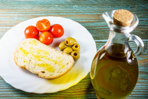 A high angle shot of olive oil with olives, tomatoes, and bread on a white plate