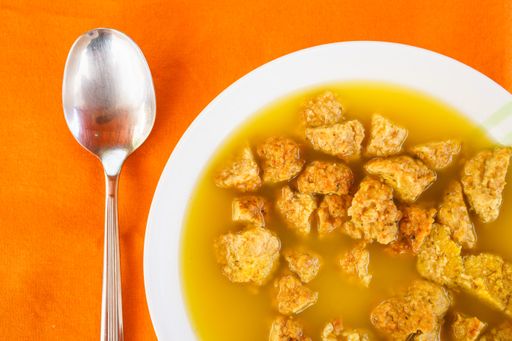 An overhead shot of a tasty bowl of soup with a spoon on the side on an orange background