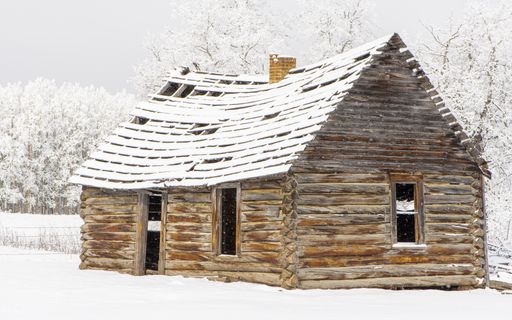An old abandoned cabin house in the field covered with snow.