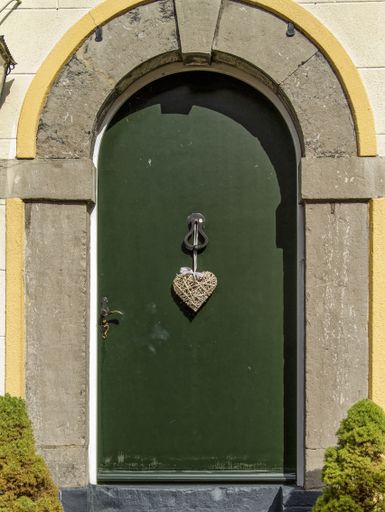 A vertical shot of an arch and a green door with a heart-shaped hanging ornament during daytime