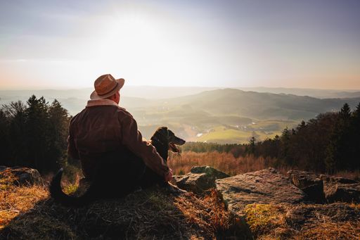 A man with a dog enjoying a beautiful view while sitting on top of a rocky mountain
