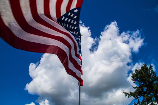 A low angle shot of the American flag in the wind against a blue sky with blue clouds