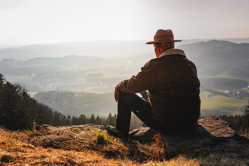 A man with a hat using a smartphone while sitting on top of a rocky mountain