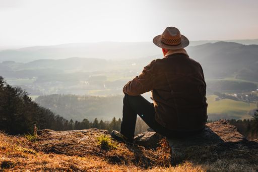 A man with a hat relaxing in the mountains during the sunrise