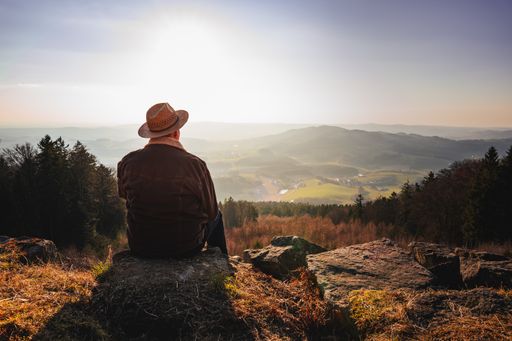 A man with a hat relaxing in the mountains during the sunrise