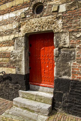 A vertical shot of an orange wooden door of a stone building during daytime