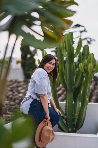 a vertical shot of woman posing with hat near cactus