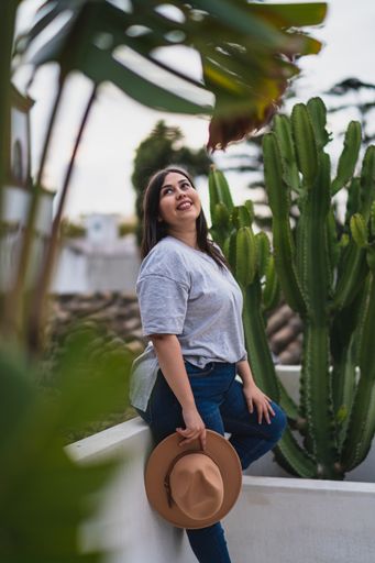a vertical shot of girl in hat on rooftop against cactus plant
