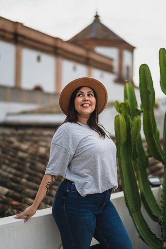 A vertical shallow focus of a caucasian young woman with a hat posing on a rooftop