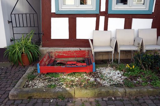 A broken palette next to some chairs placed next to a house in the yard.