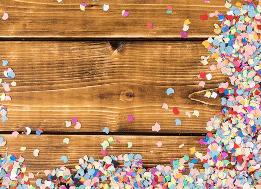 A top view of multicolored confetti and streamers on a wooden table