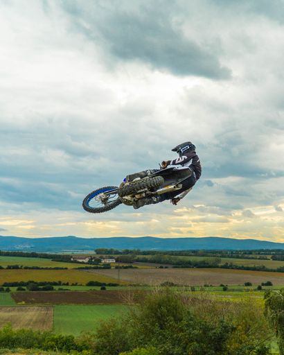 A vertical shot of a motorcycle jumping over a ramp against a blue sky