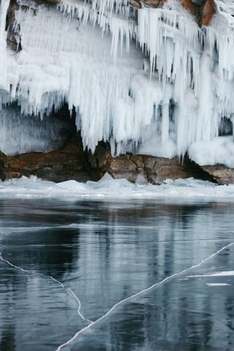 A vertical shot of a frozen body of water against a cliff with big iciles