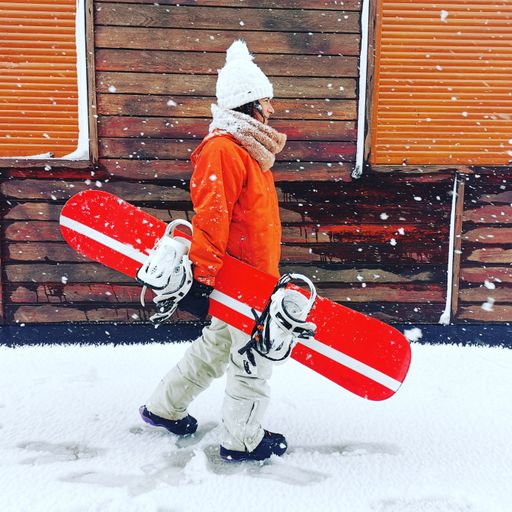 A woman in warm clothes holding a snowboard