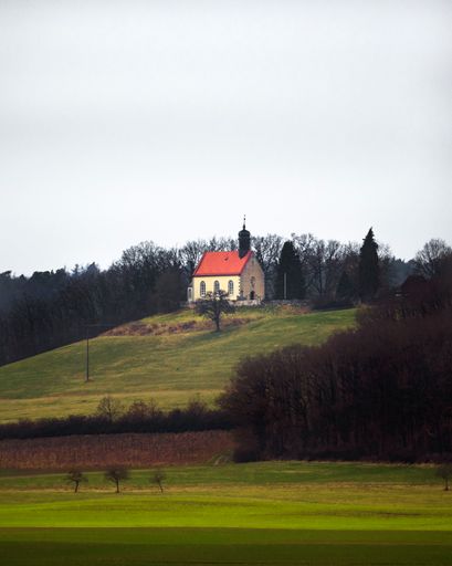 A vertical shot of a small chapel on a green hill