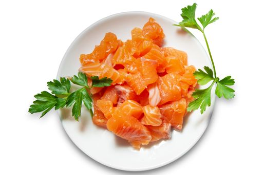 A top shot of cut salmon pieces served with parsley leaves on a plate.