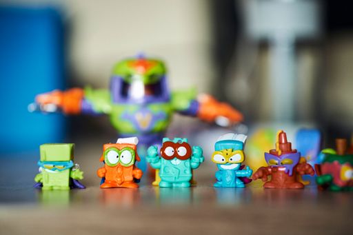 A close-up shot of a row of plastic Magic Box brand Superthings toy figurines standing on a wooden table