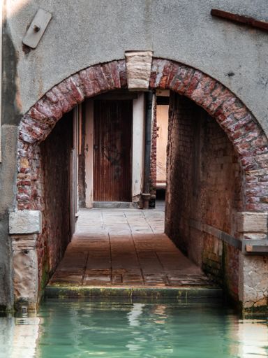 A vertical shot of narrow alleyway with stone arch through Venetian lagoon in Venice, Italy