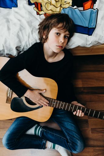 A young fair-haired boy sitting on the floor and holding a guitar