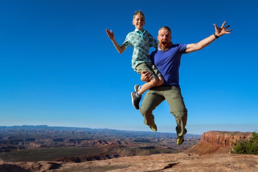 A father jumping with his son in his hands in Canyonlands national park on a blue sky background