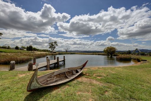 The old wooden boat on the green lakeside against the background of blue sky with white clouds. Mudgee, Australia.