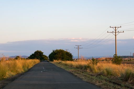 An asphalt road near an old railway during a sunset