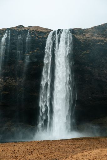 A vertical shot of a waterfall coming out of a huge cliff.