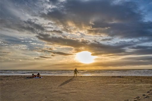 Man metal detecting on Cocoa Beach, FL.  Two women on beach towels watching sunrise on a cloudy morning.