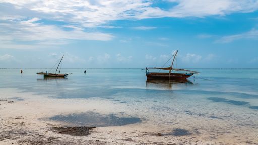 A scenic view of sailboats near the beach in Zanzibar on a blue cloudy sky background