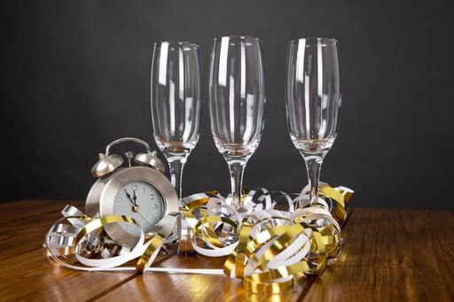 A empty glasses behind a clock among colorful confetti near gray wall - concept of waiting new year