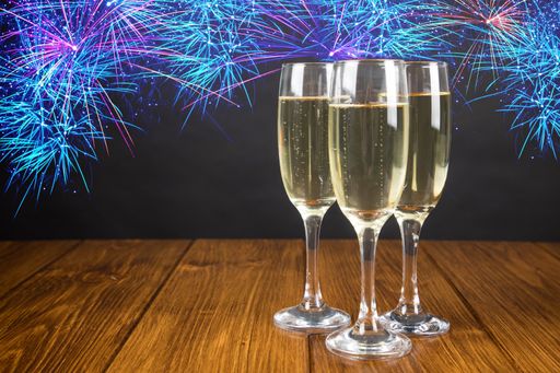 A glasses with champagne on a wooden table near gray wall with firework illustrations