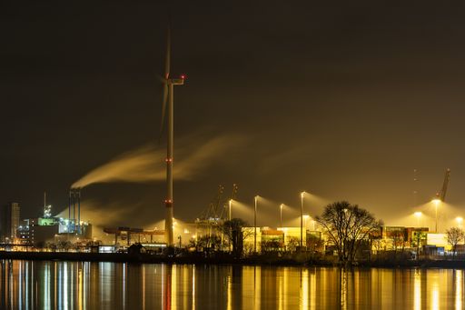 A horizontal shot of a lot of water sprinklers on the shore near the buildings at night time