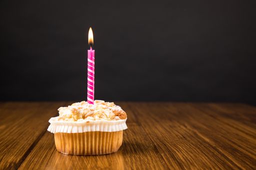 A muffin with burning candle on a wooden table near gray wall with space for text