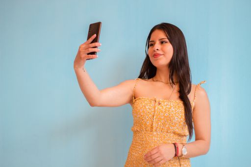 A closeup of a young woman in a summer outfit taking selfie isolated on light blue background.