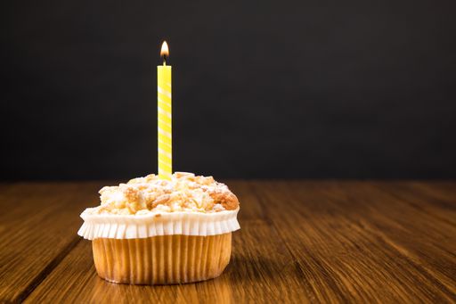 A muffin with burning candle on a wooden table near gray wall with space for text