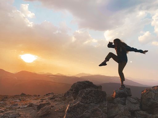 A closeup of a girl standing on a rock with sunset in the background