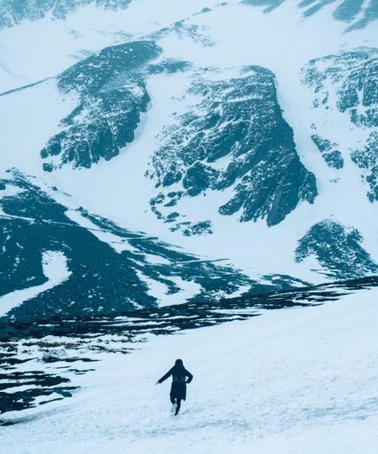 a vertical shot of man running in snow against snow covered mountain