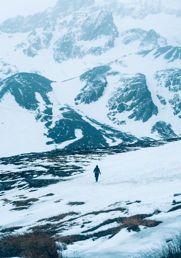 a vertical shot of man running in snow against snow covered mountain