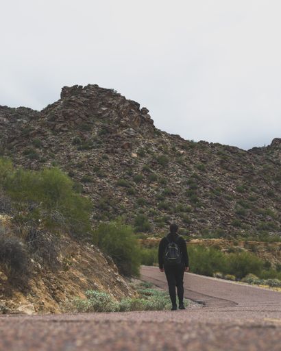 A back view of a tourist on a road with hills on a cloudy day