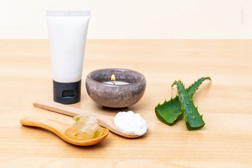 A close-up shot of cream tube, Aloe-Vera green peels, Aloe-Vera jell and white cream in wooden spoons on a wooden table with blurred background