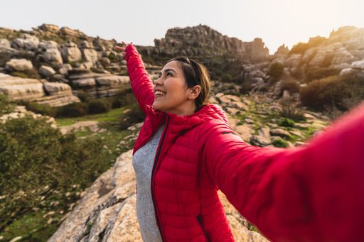 A beautiful shot of a Caucasian girl with red jacket smiling while taking a selfie with her camera in El Torcal de Antequera, Malaga, Spain
