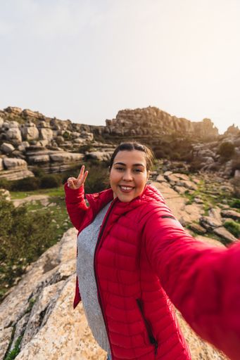 A beautiful shot of a Caucasian girl with red jacket smiling while taking a selfie with her camera in El Torcal de Antequera, Malaga, Spain