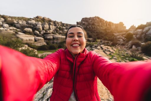 A beautiful shot of a Caucasian girl with red jacket smiling while taking a selfie with her camera in El Torcal de Antequera, Malaga, Spain