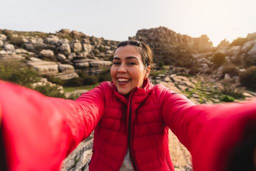 A beautiful shot of a Caucasian girl with red jacket smiling while taking a selfie with her camera in El Torcal de Antequera, Malaga, Spain