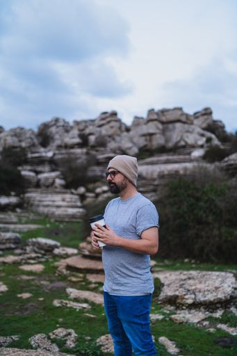A beautiful shot of an adult Caucasian man holding his coffee while standing in El Torcal de Antequera during daytime, Malaga, Spain